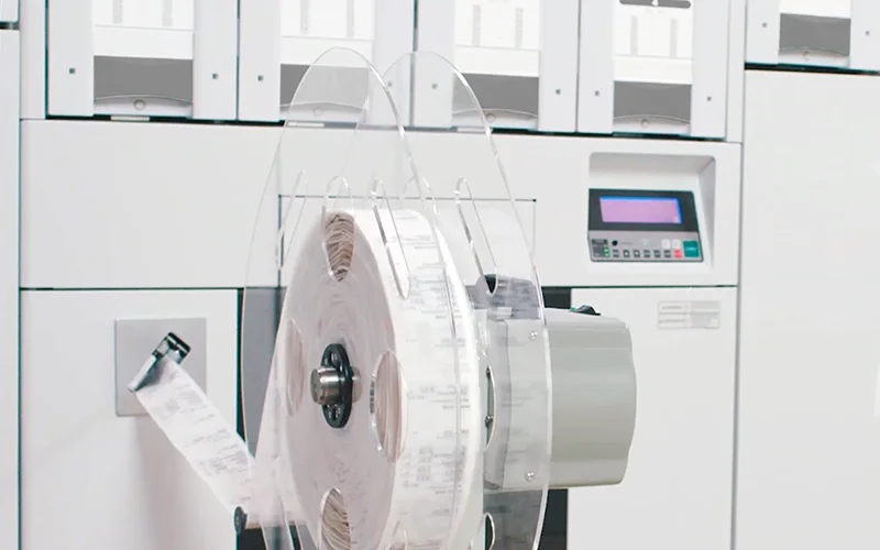 A strip of sealed medication pouches feeding out of an automated pouch packager
